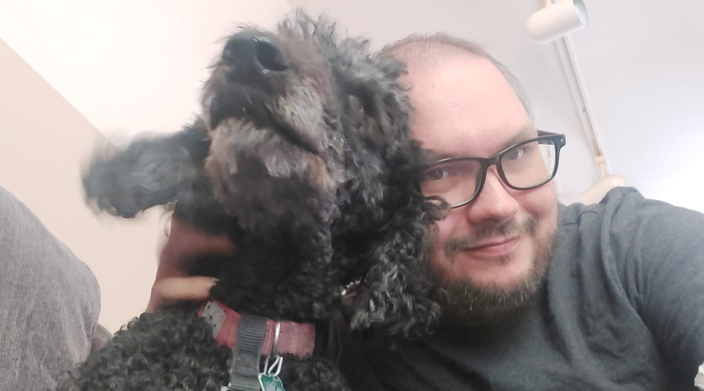 A man sits next to a black standard poodle, her ears look like wings as she moves quickly